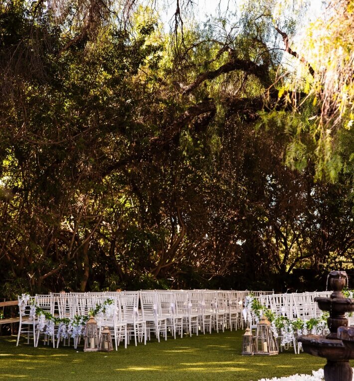 Outdoor wedding ceremony seating decorated with greenery and lanterns