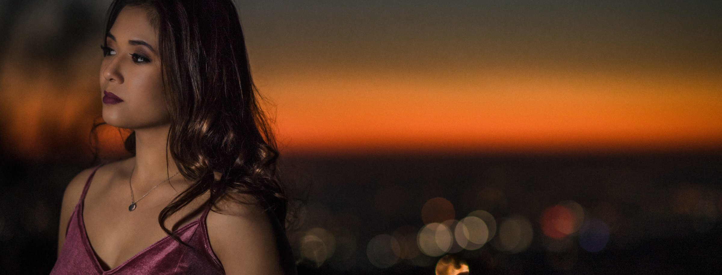 High school senior girl in a velvet dress at dusk with city lights behind her, senior portrait by Los Angeles senior photographer Renee Bowen