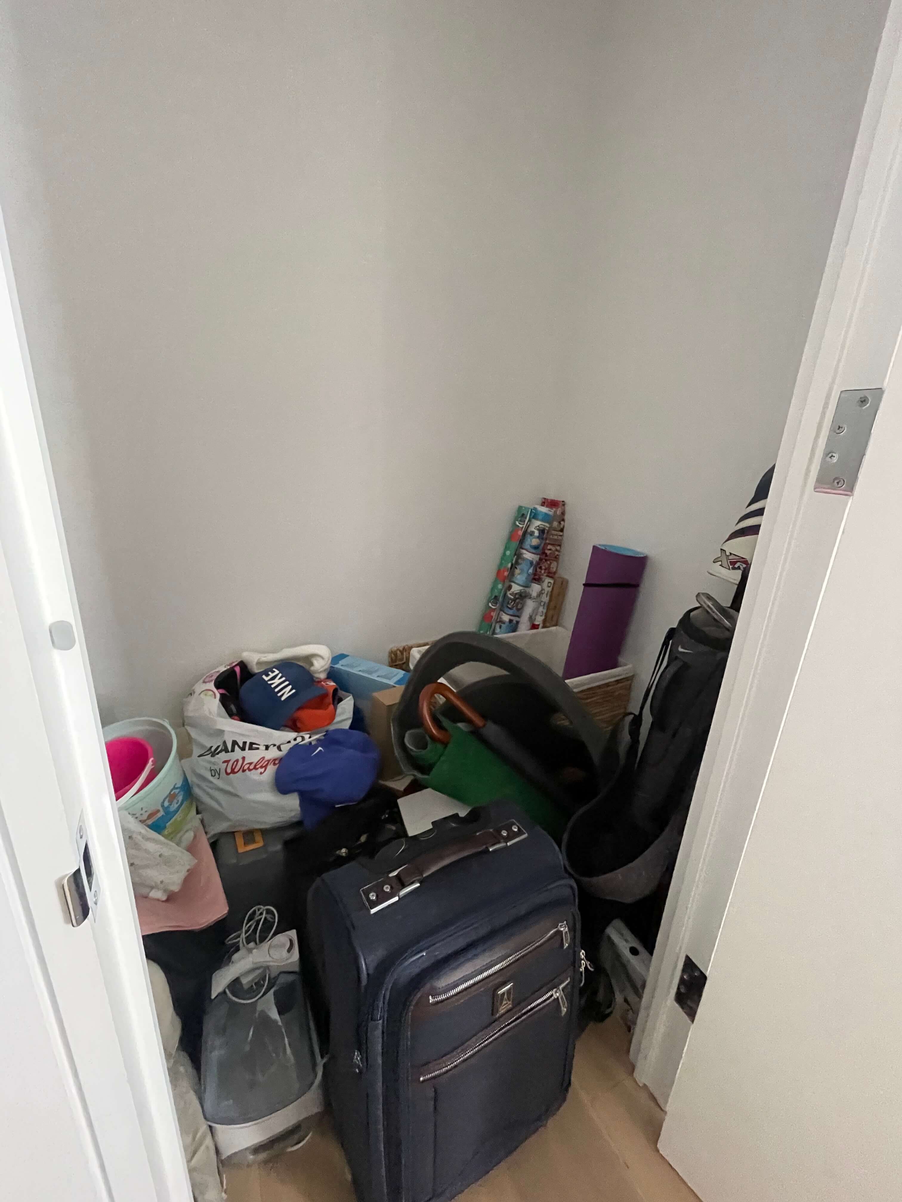 Cluttered storage closet with luggage, bags, and household items piled on the floor.