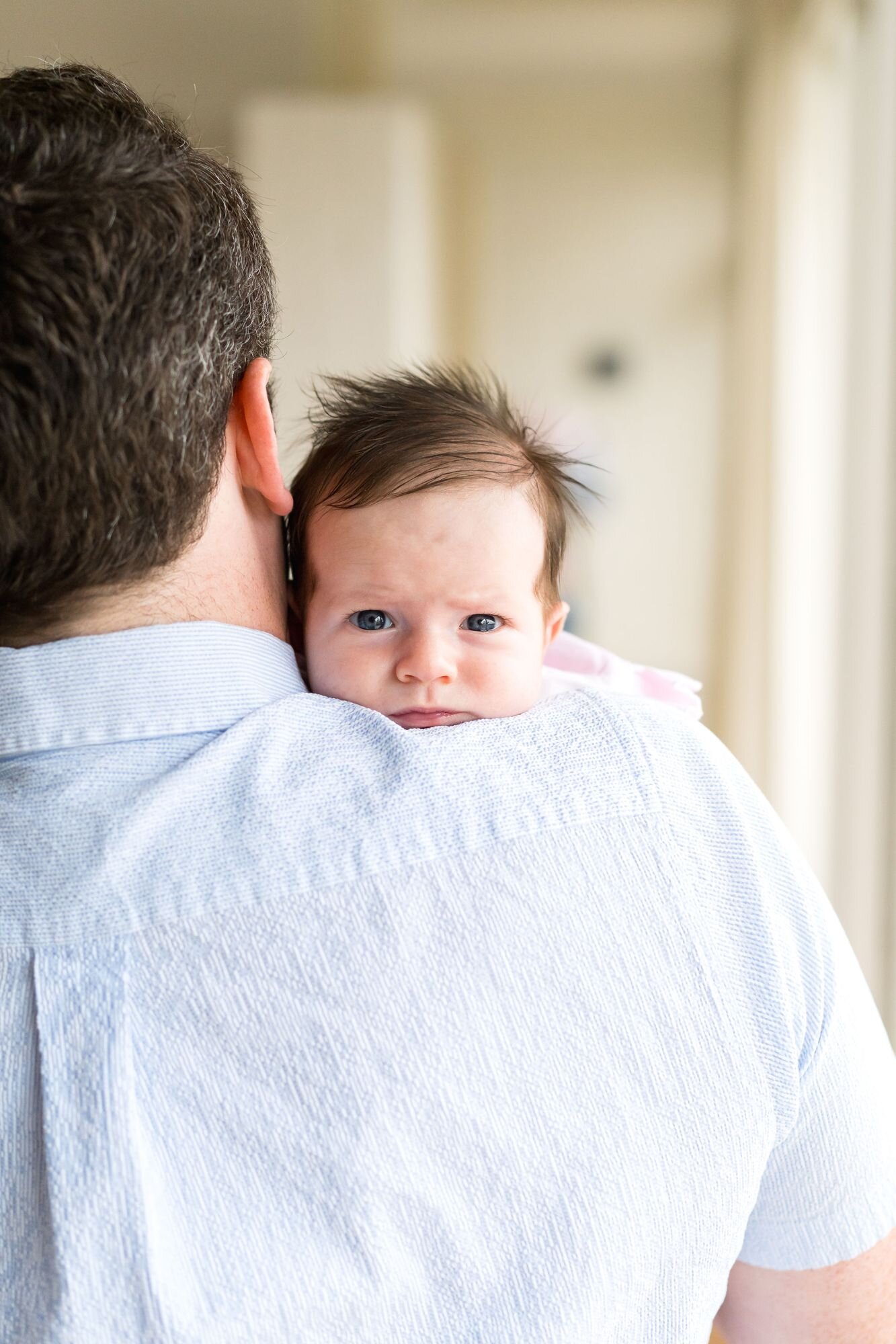 Wide-eyed newborn peeking over dad's shoulder at home