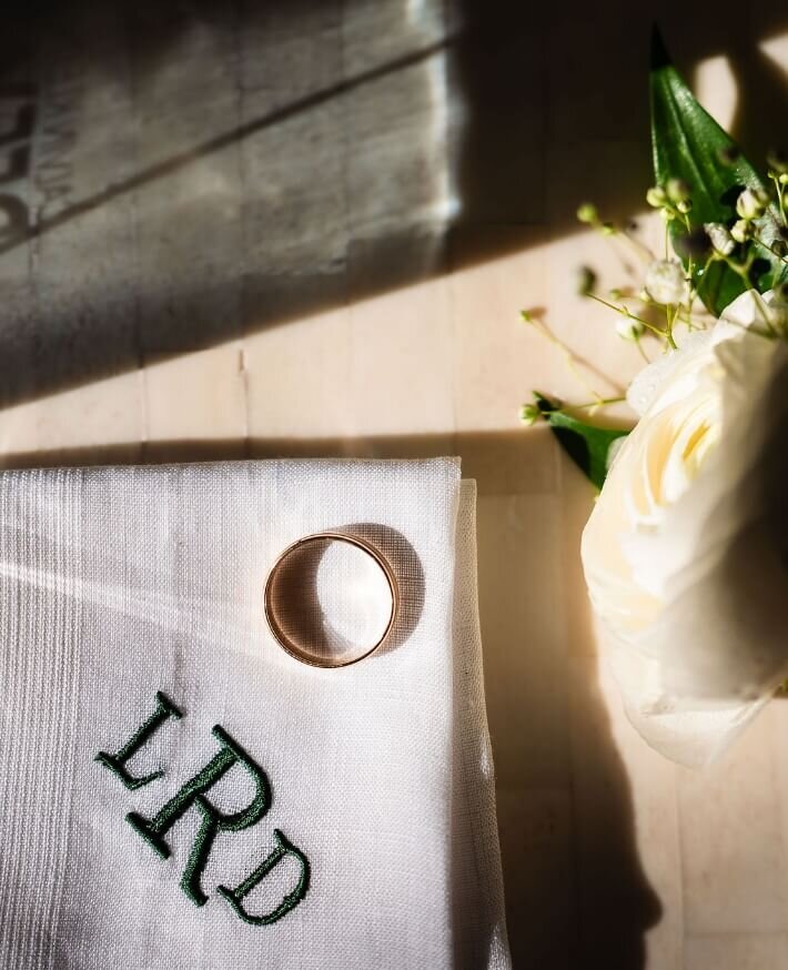 Wedding bands on a monogrammed handkerchief beside a white rose