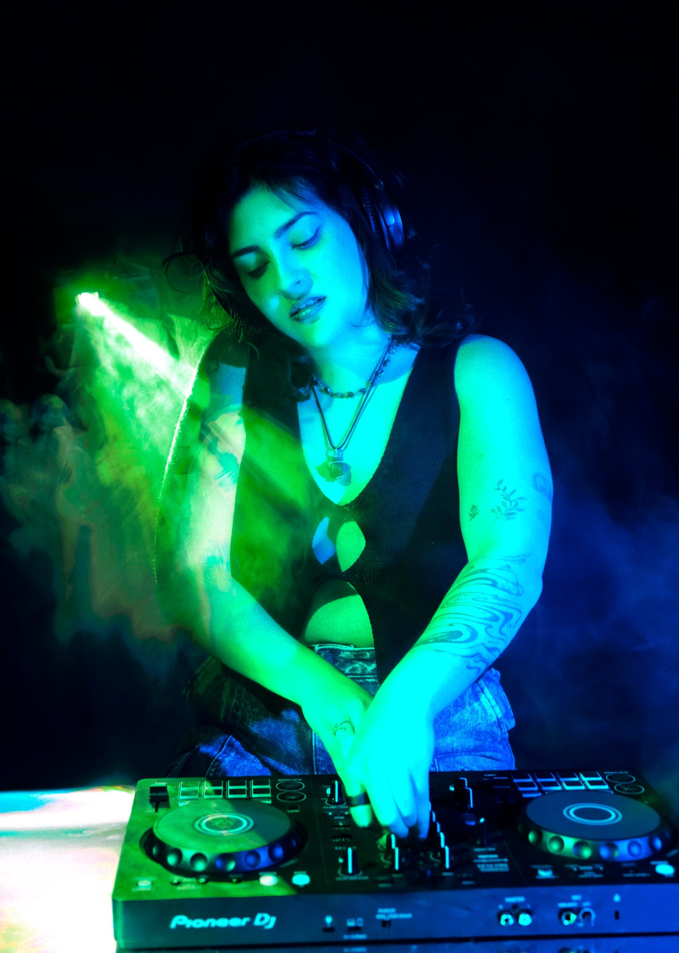 Woman poses with her DJ equipment under strobe lights.