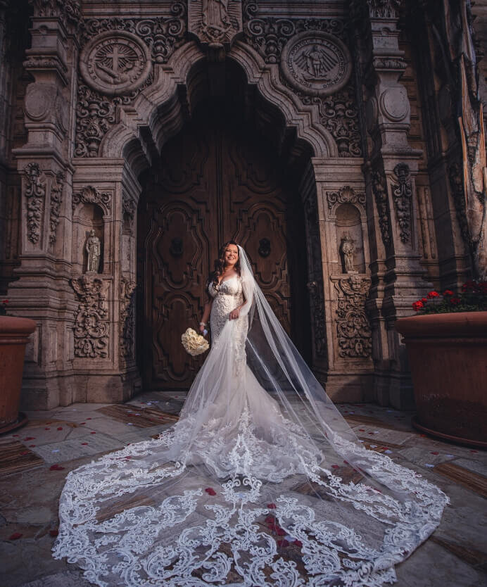 Bride displaying her long lace train in front of an ornate doorway