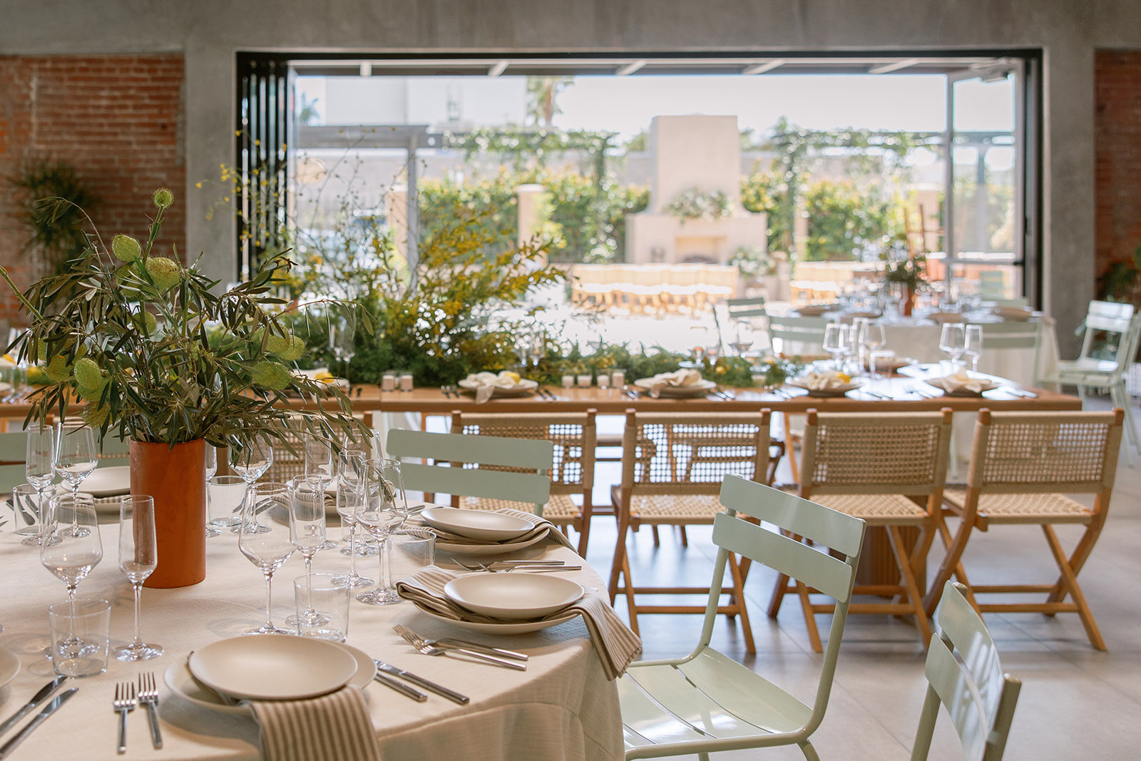 A layered indoor tablescape with neutral linens and mixed chairs overlooking Palomino’s patio through open doors.