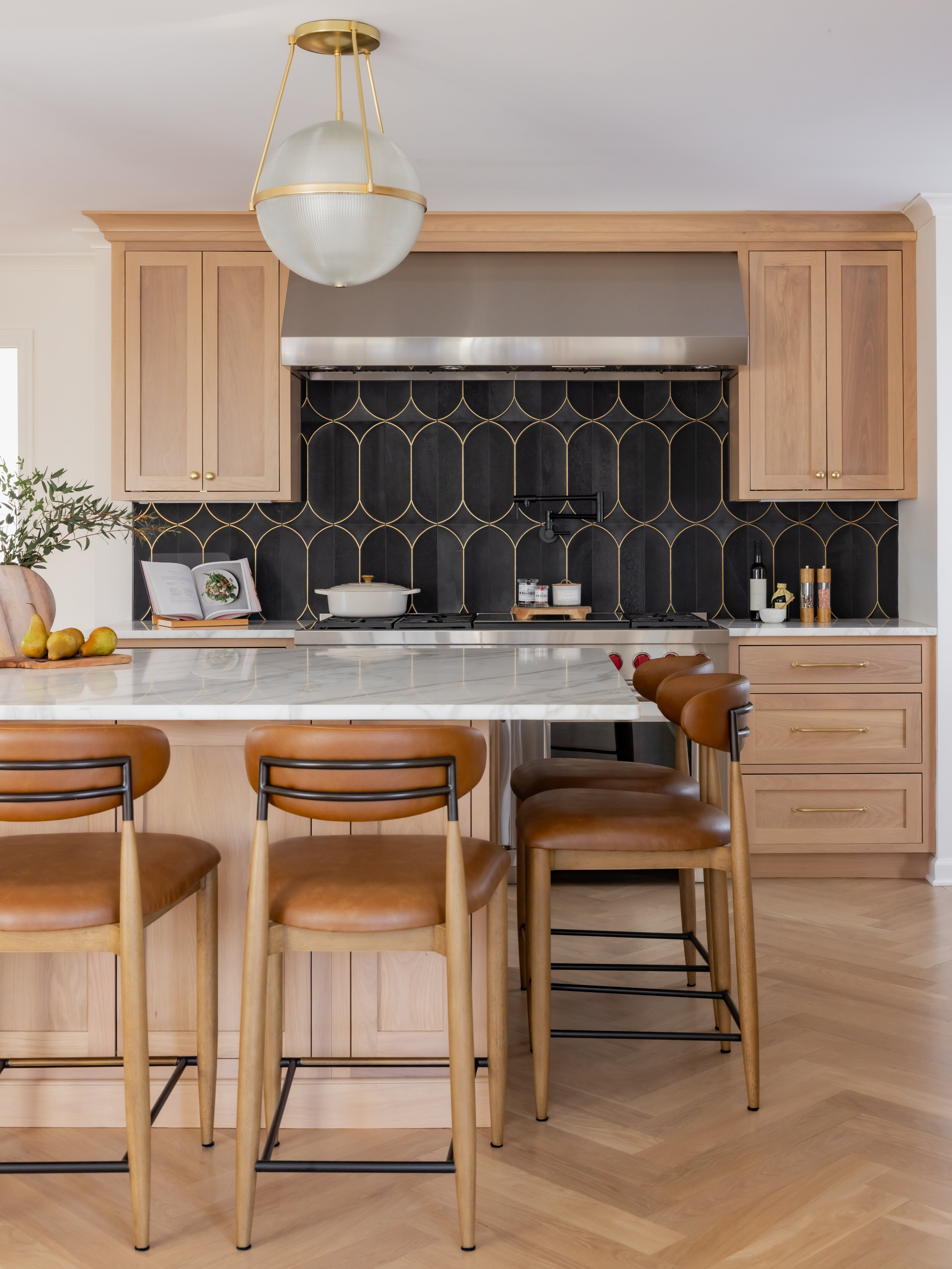 Renovated kitchen with white oak cabinetry, a dark scalloped tile backsplash, a globe pendant light, and leather counter stools at a marble island