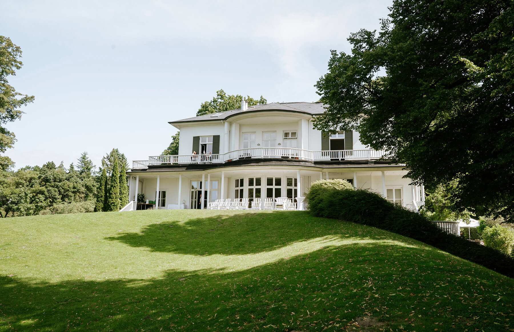 Braut im Profil mit langem Schleier, den weißen Rosenstrauß sanft am Gesicht; natürliche hochzeitsfotografie und fine art hochzeitsfotografie im blühenden Garten