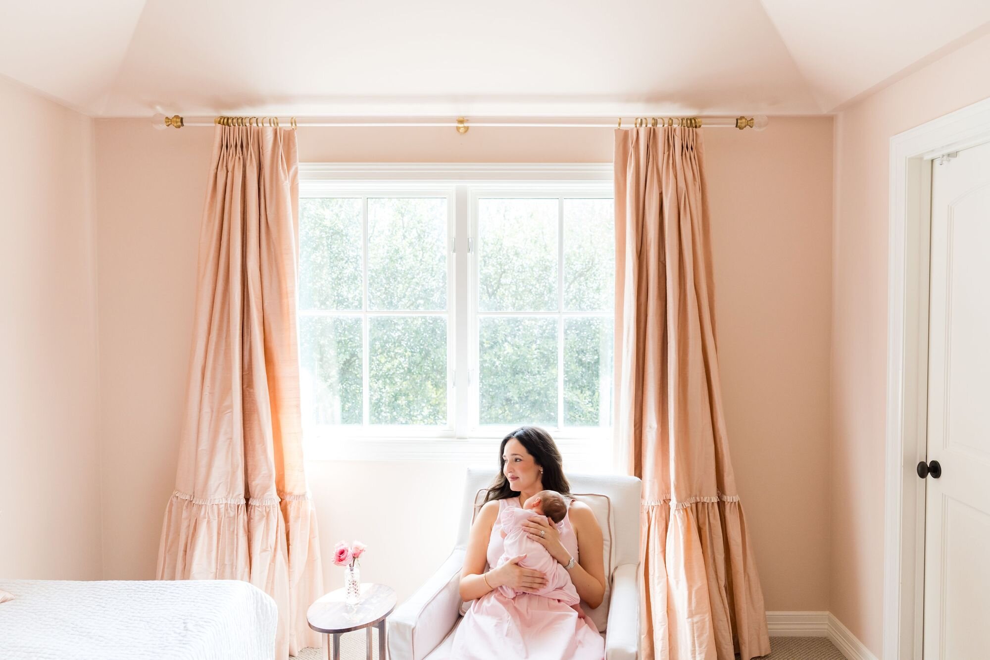 Mom holding her newborn in a rocking chair by the nursery window during an in-home newborn session in Austin