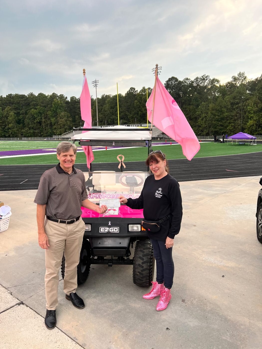 Mark Galvin of CPG hands Alice Ramsey a donation check by the Pink Posse golf cart