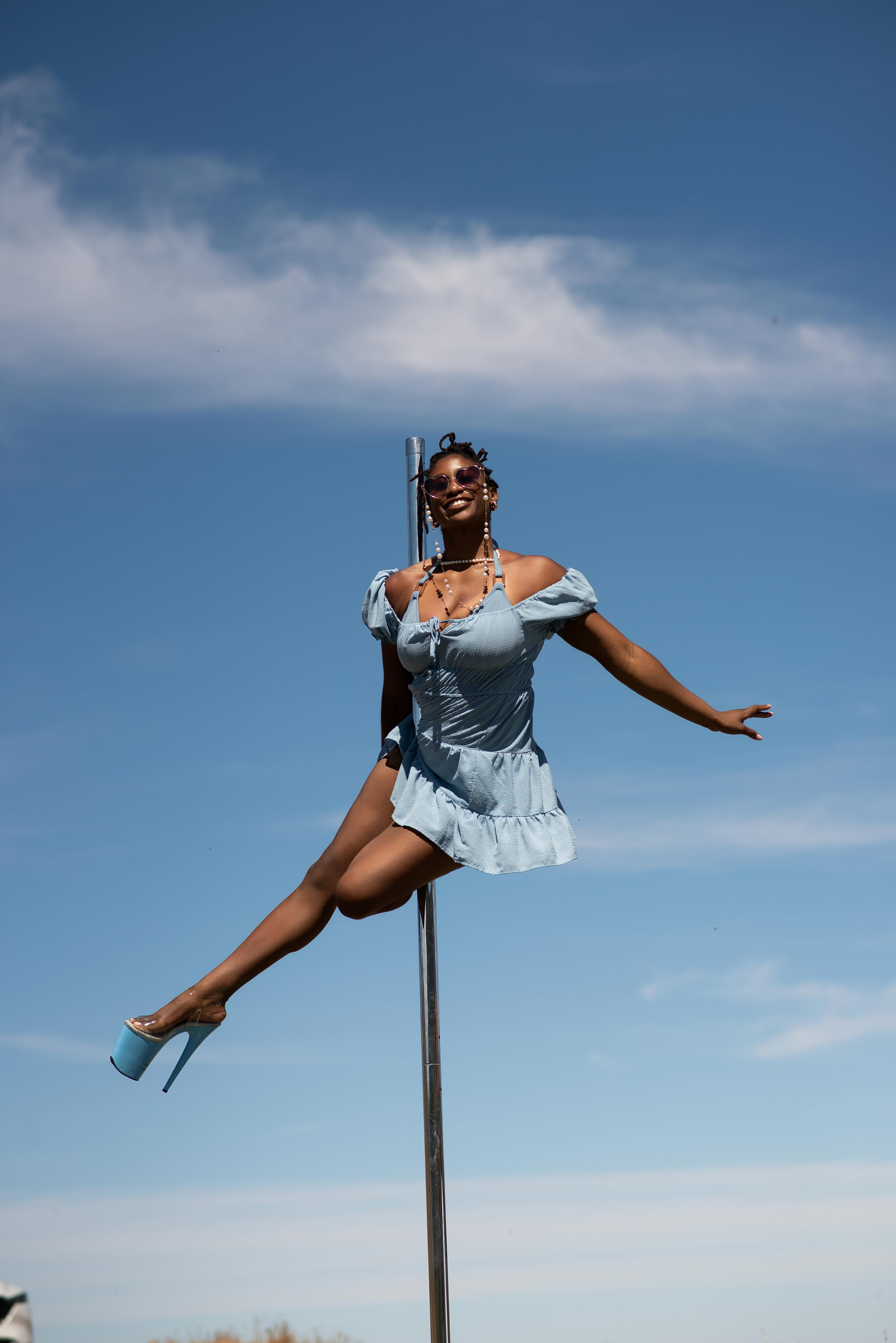 Pole dancer creating a strong shape beneath a blue sky