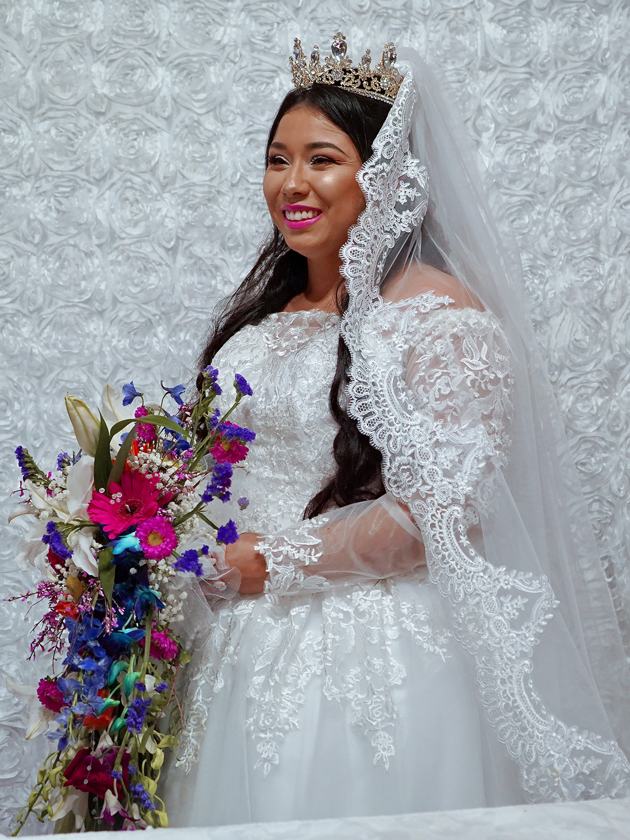 Bride wearing a crown and lace veil while holding a colorful cascading bouquet