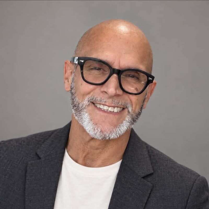 Roberto Estremera smiling, wearing black glasses and a charcoal jacket