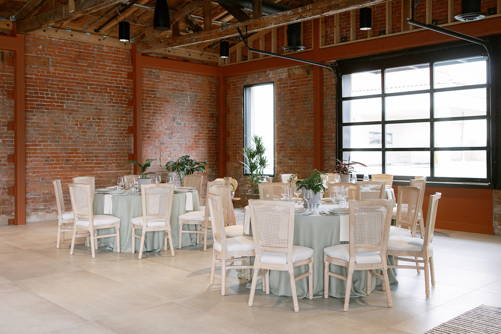 Round reception tables with sage linens and cane-back chairs arranged inside Palomino’s brick-walled venue.