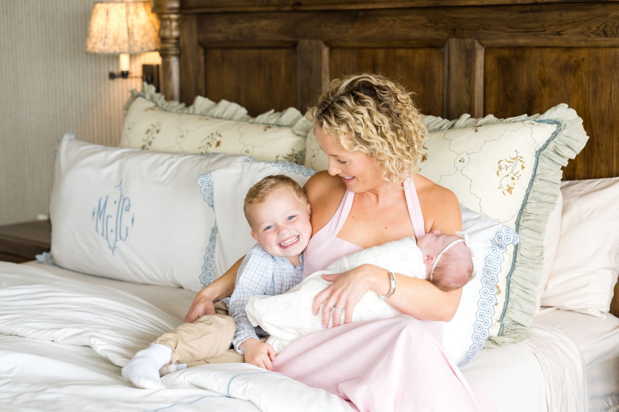 Laughing big brother snuggling mom and his newborn sibling on the bed