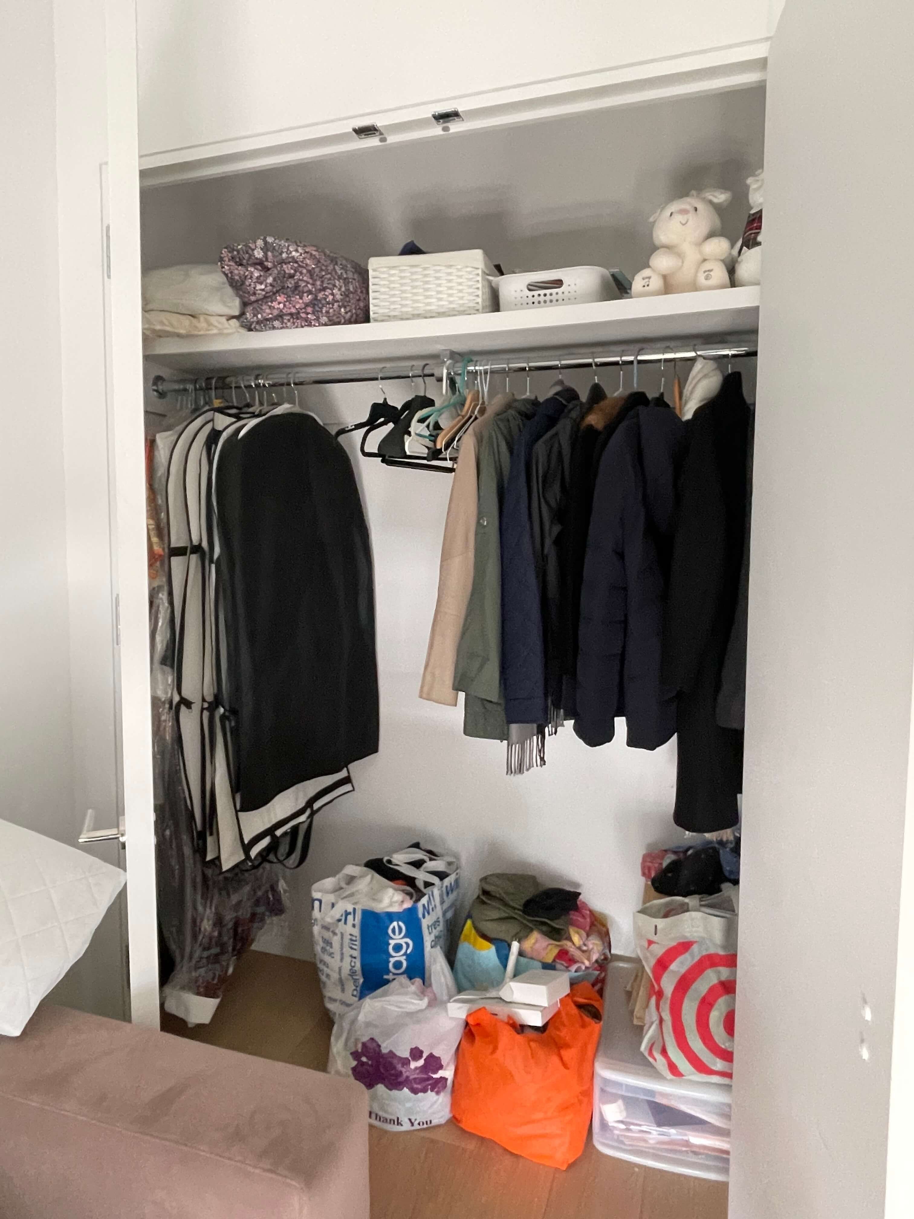 Cluttered bedroom closet with hanging clothes, bedding, and miscellaneous storage items.