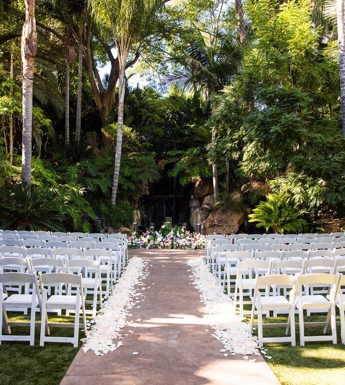 Southern California outdoor wedding ceremony with white chairs and flower petals