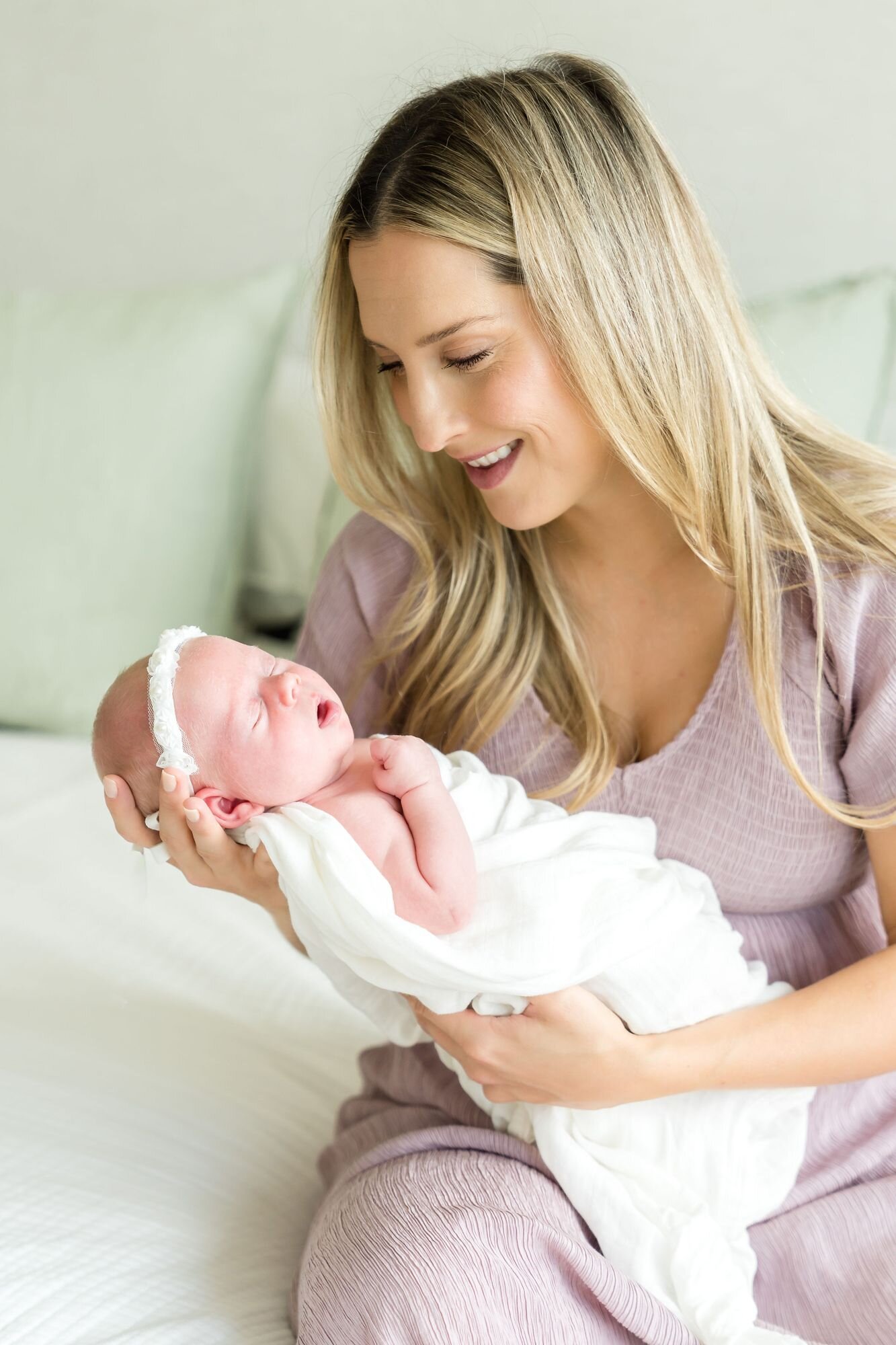 Smiling mom cradling her newborn daughter on the bed during an in-home newborn session
