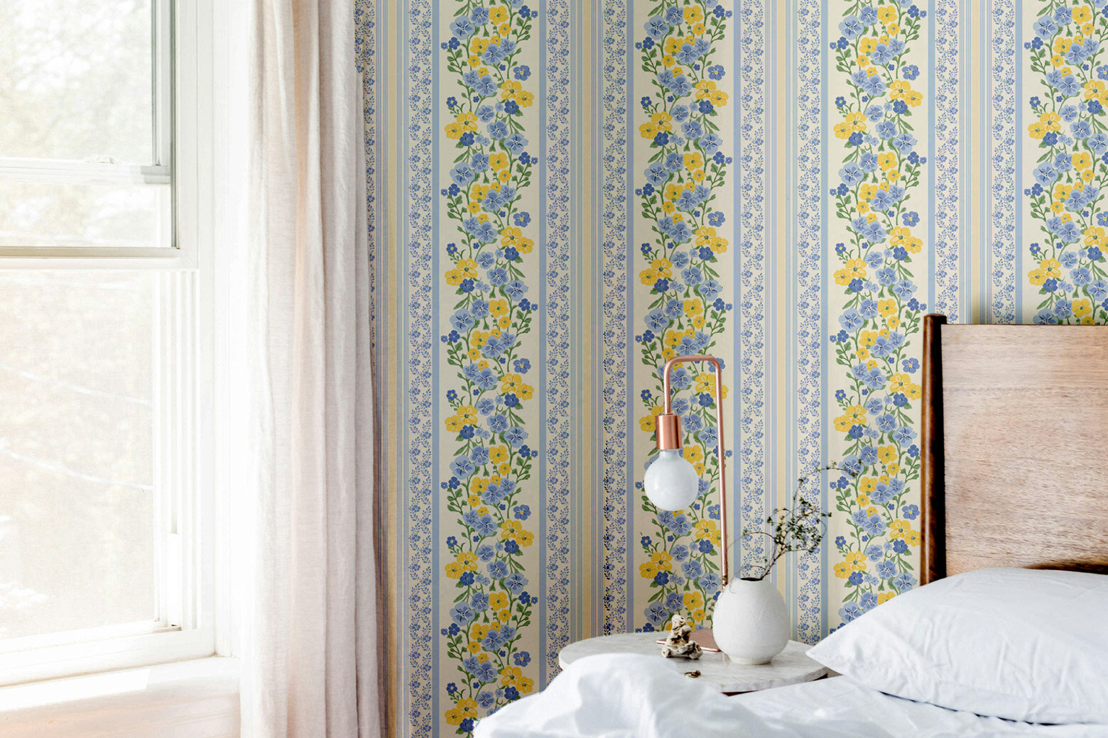 Blue and yellow cottage floral stripe wallpaper in a bedroom with natural oak headboard and white bedding