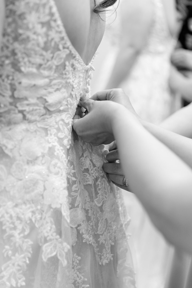 Black and white wedding dress detail with hands fastening bridal buttons.