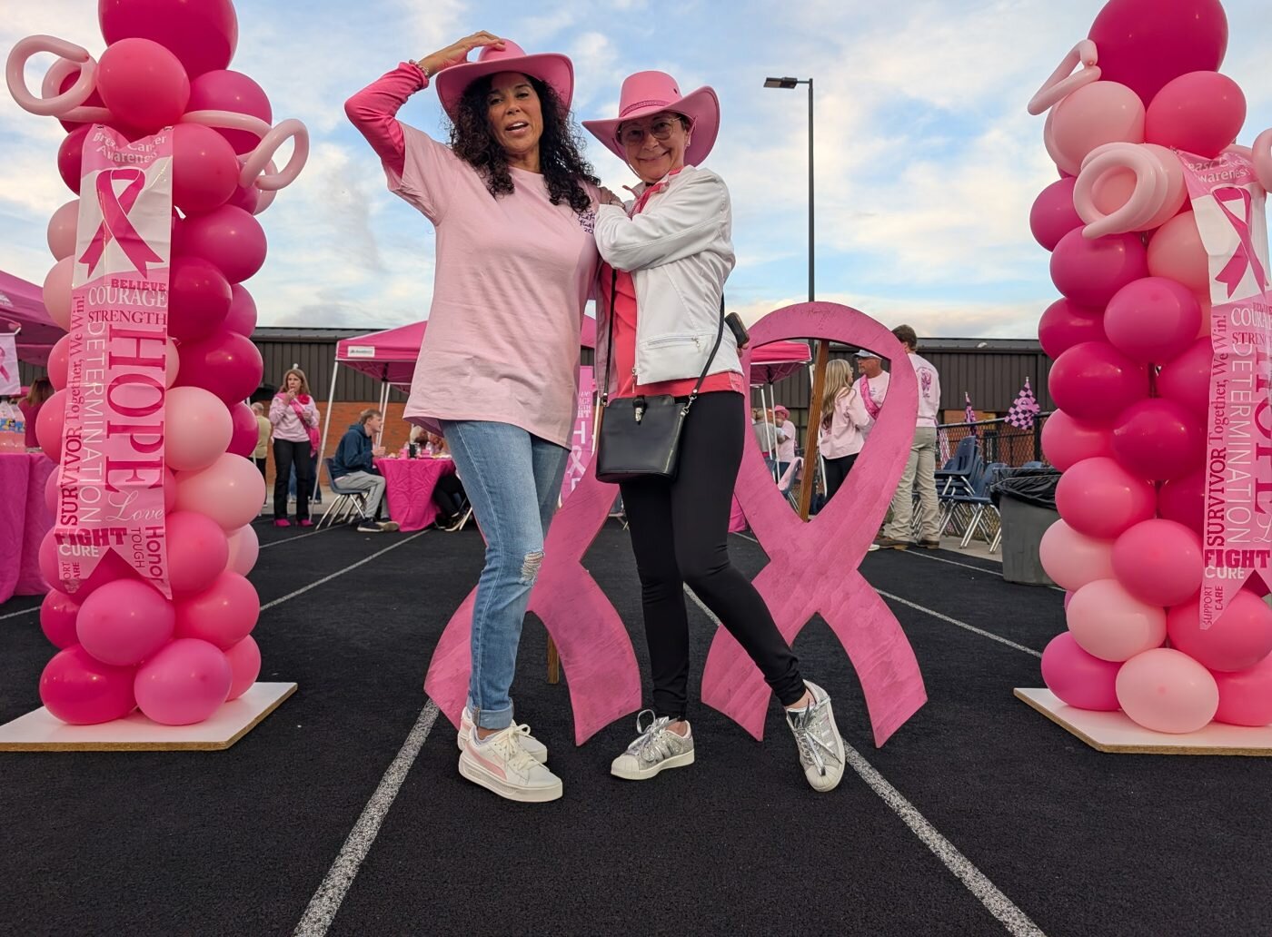 Two women in pink cowboy hats with a giant pink ribbon