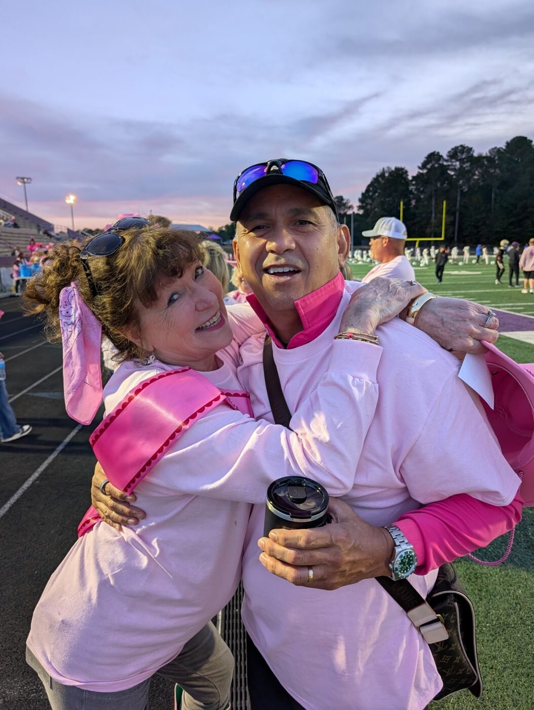 Chip Doss of CPG hugs a guest in a pink sash on the football field