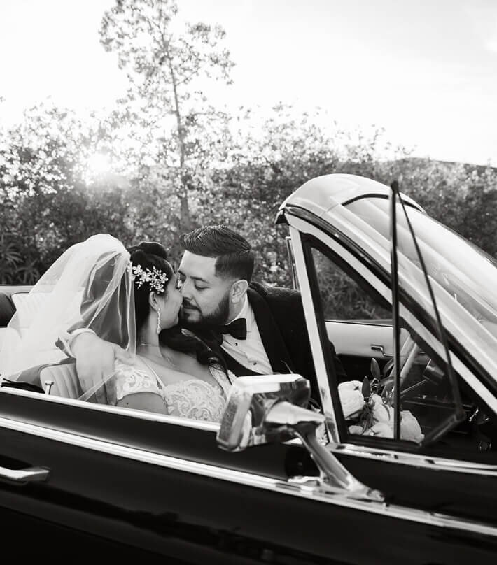 Newlyweds kissing inside a vintage car in black and white