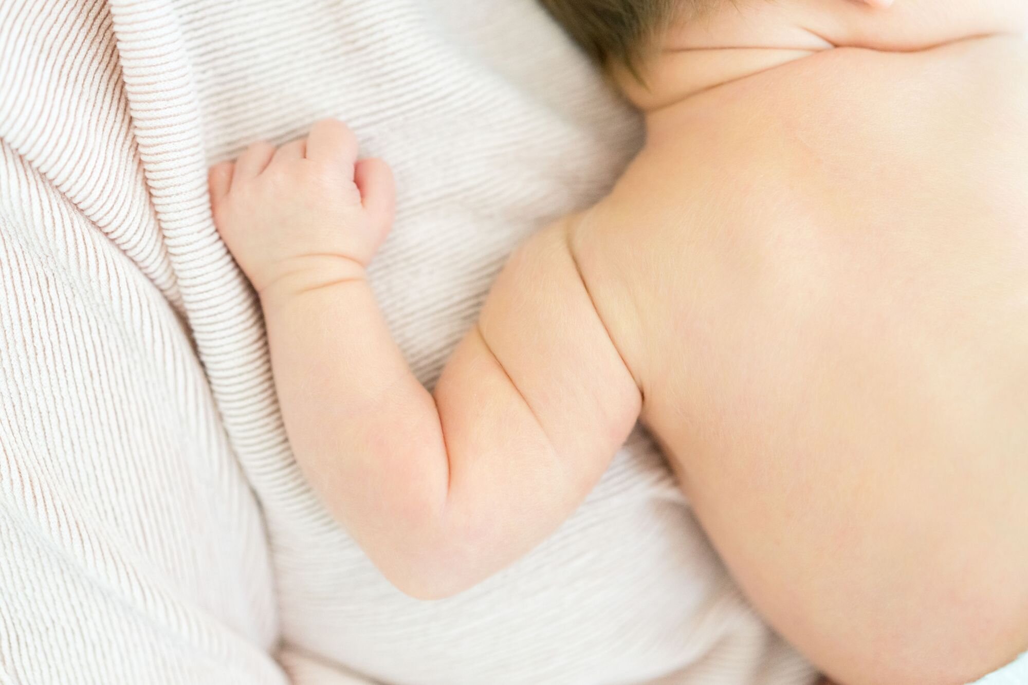 Close-up of a newborn baby's tiny hand and arm on a striped blanket
