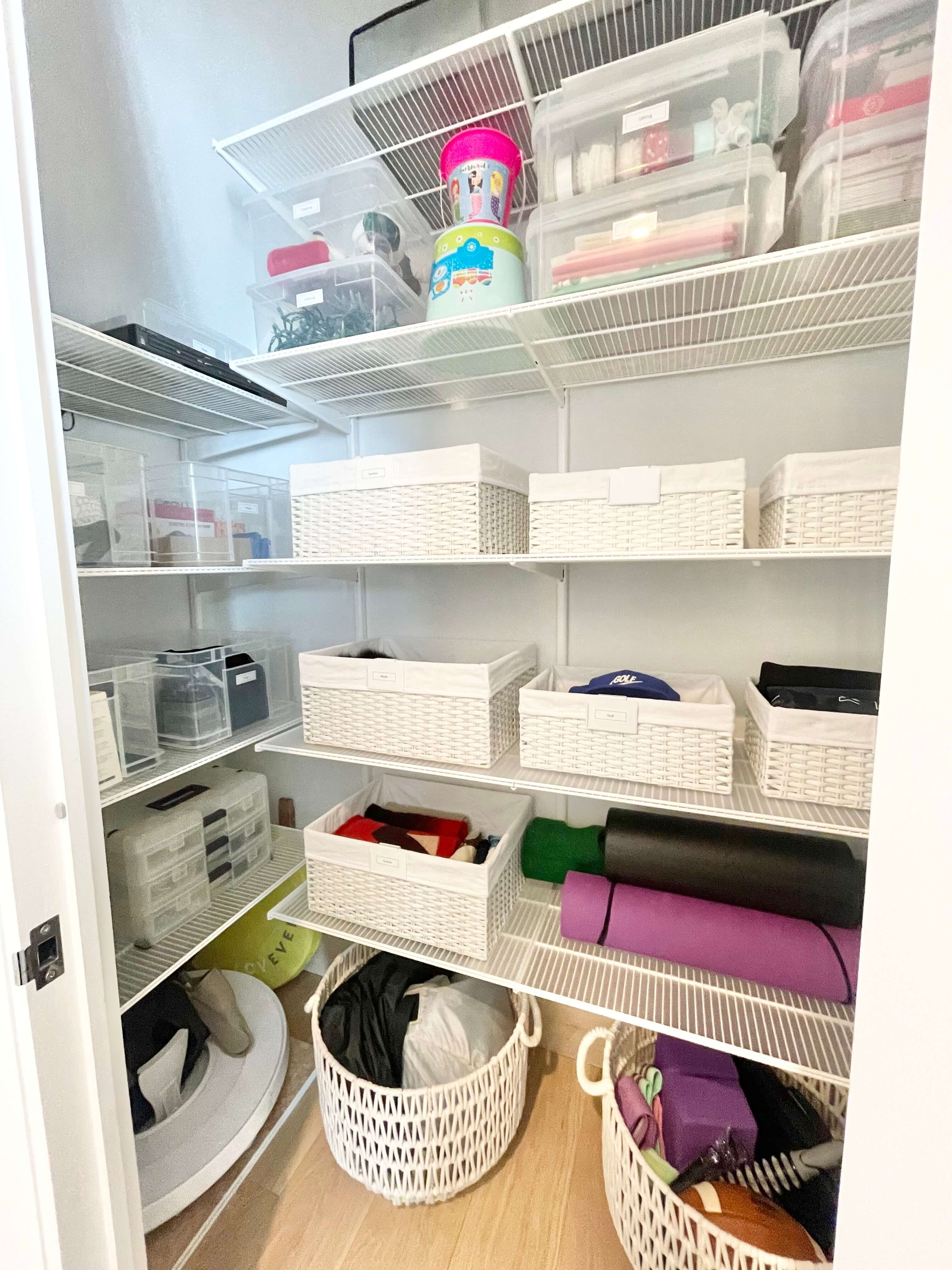 Organized storage closet with labeled baskets, clear bins, and exercise equipment on shelves.