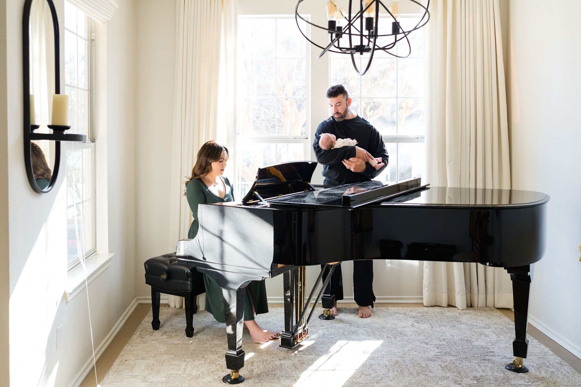 Mom playing piano while dad holds their newborn in a sunlit Austin living room