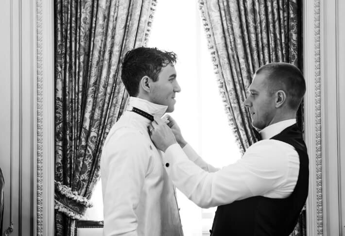 Groomsman adjusting the groom’s collar in black and white