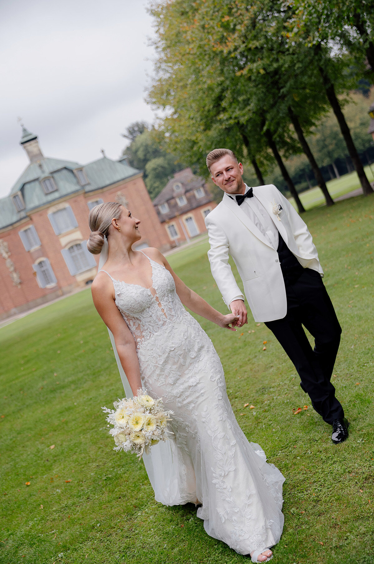 Eng umschlungen steht das Paar im sonnigen Garten unter einem Papierparasol, zarte Beete dahinter; fotograf für sommerhochzeit, natürliche hochzeitsfotografie und pärchenshooting hochzeit
