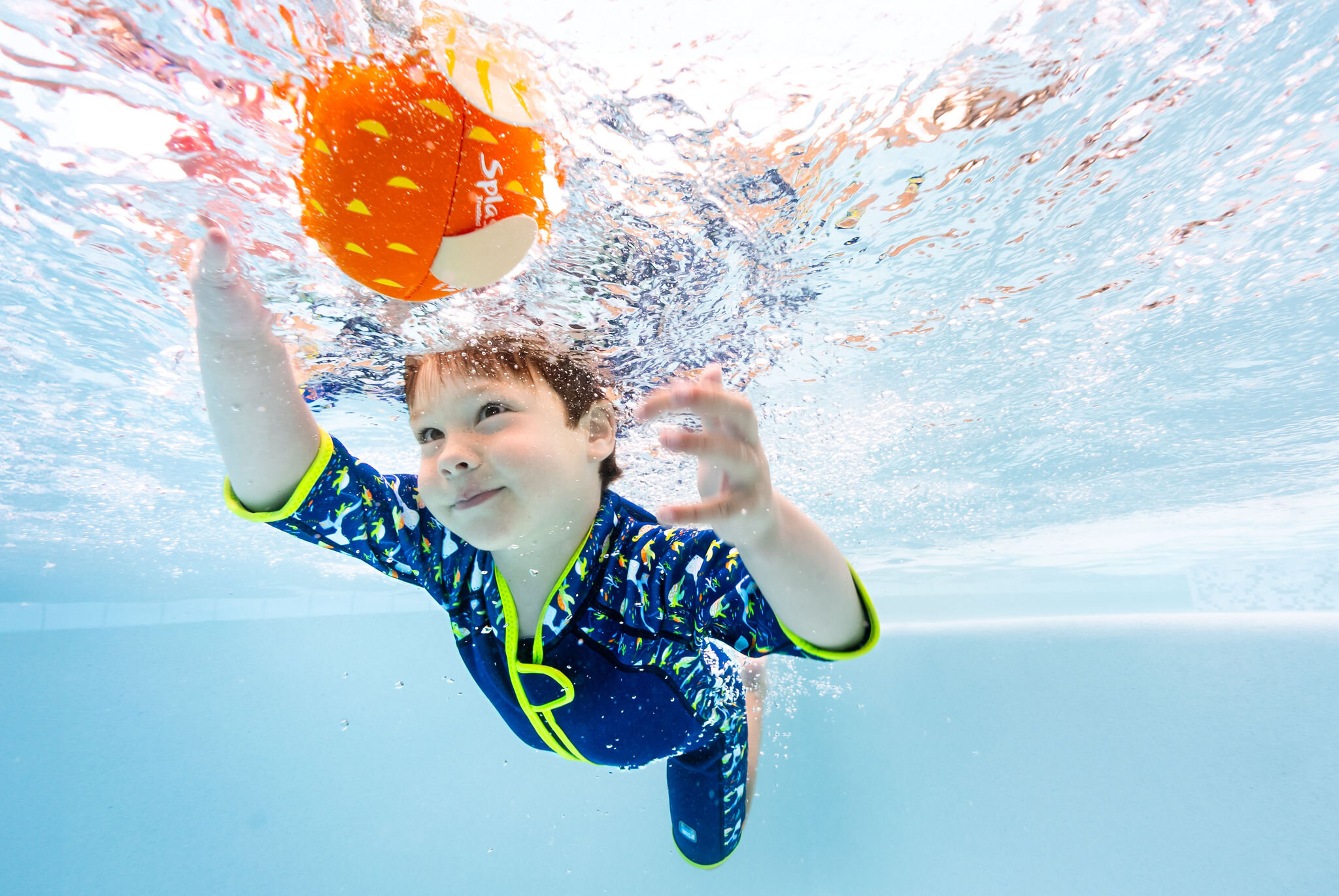 Underwater photography of a boy playing with an orange ball for Splash About
