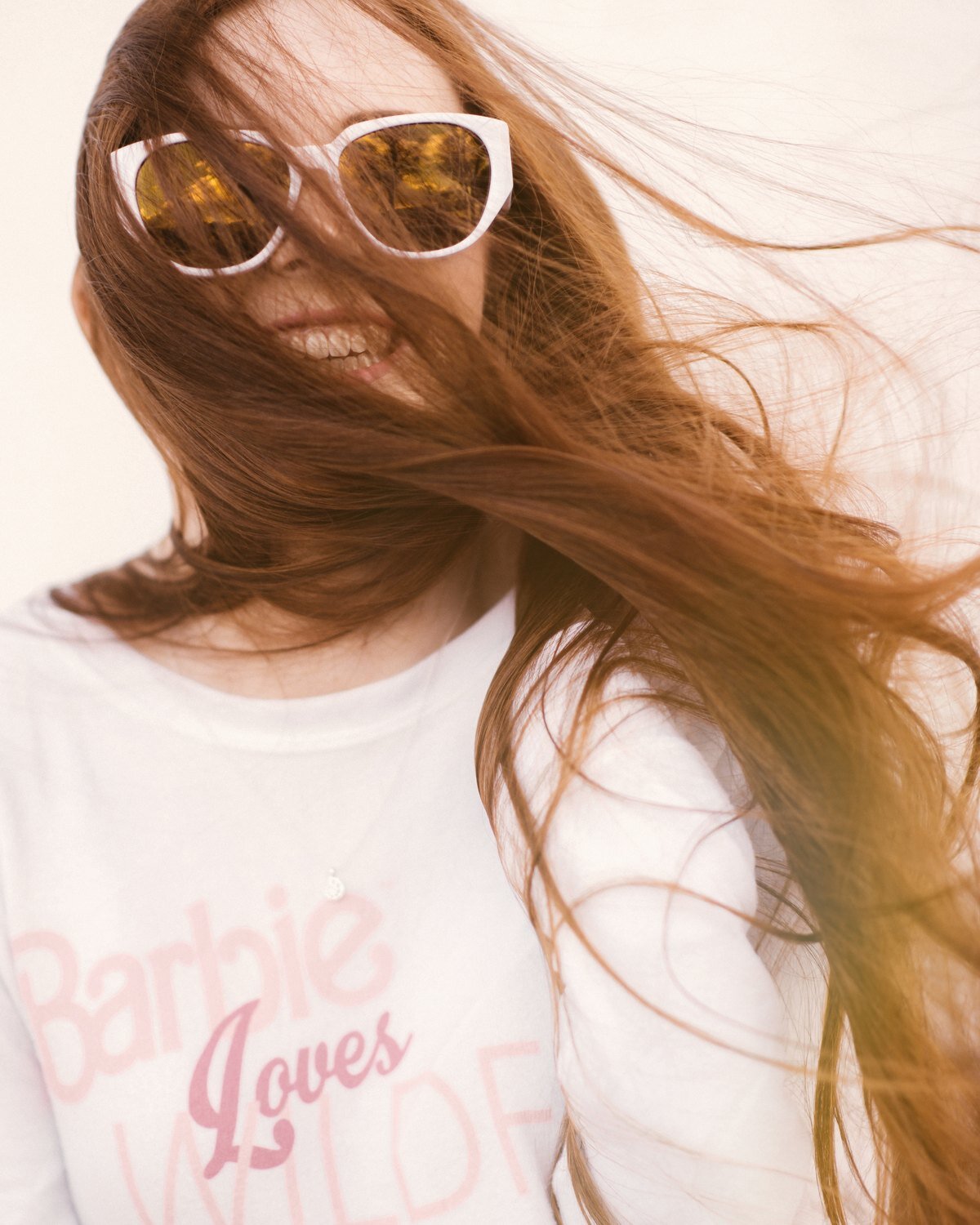 Red-haired high school senior in white sunglasses with windblown hair, senior portrait by Renee Bowen