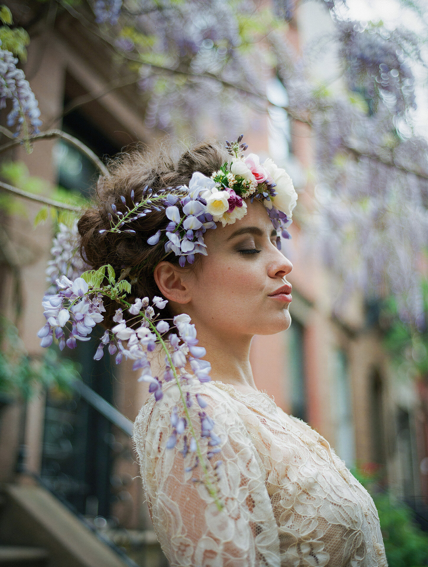 Bride in lace framed by hanging wisteria and soft city garden bokeh