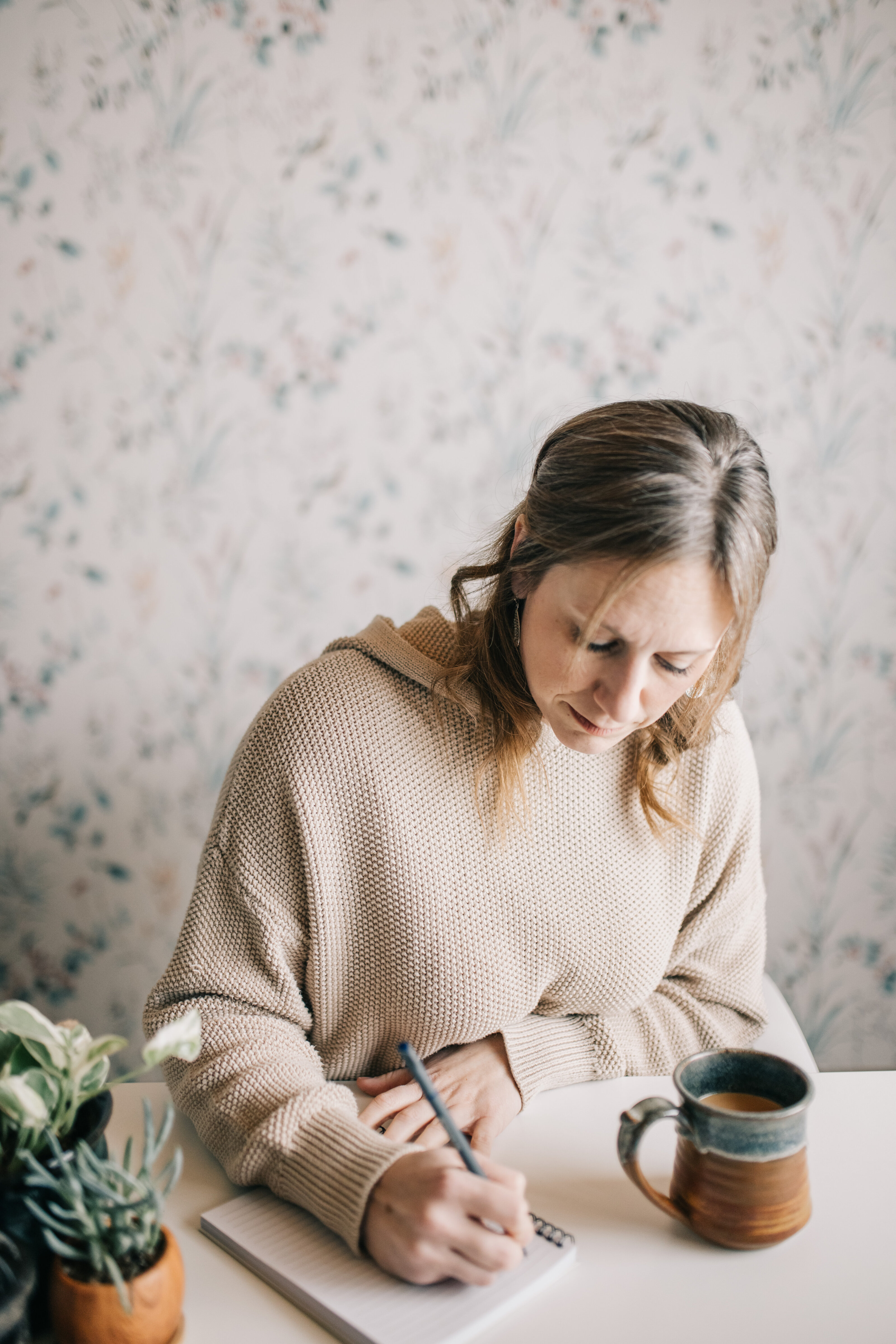 Emily McNiel writing in a notebook with a mug of coffee