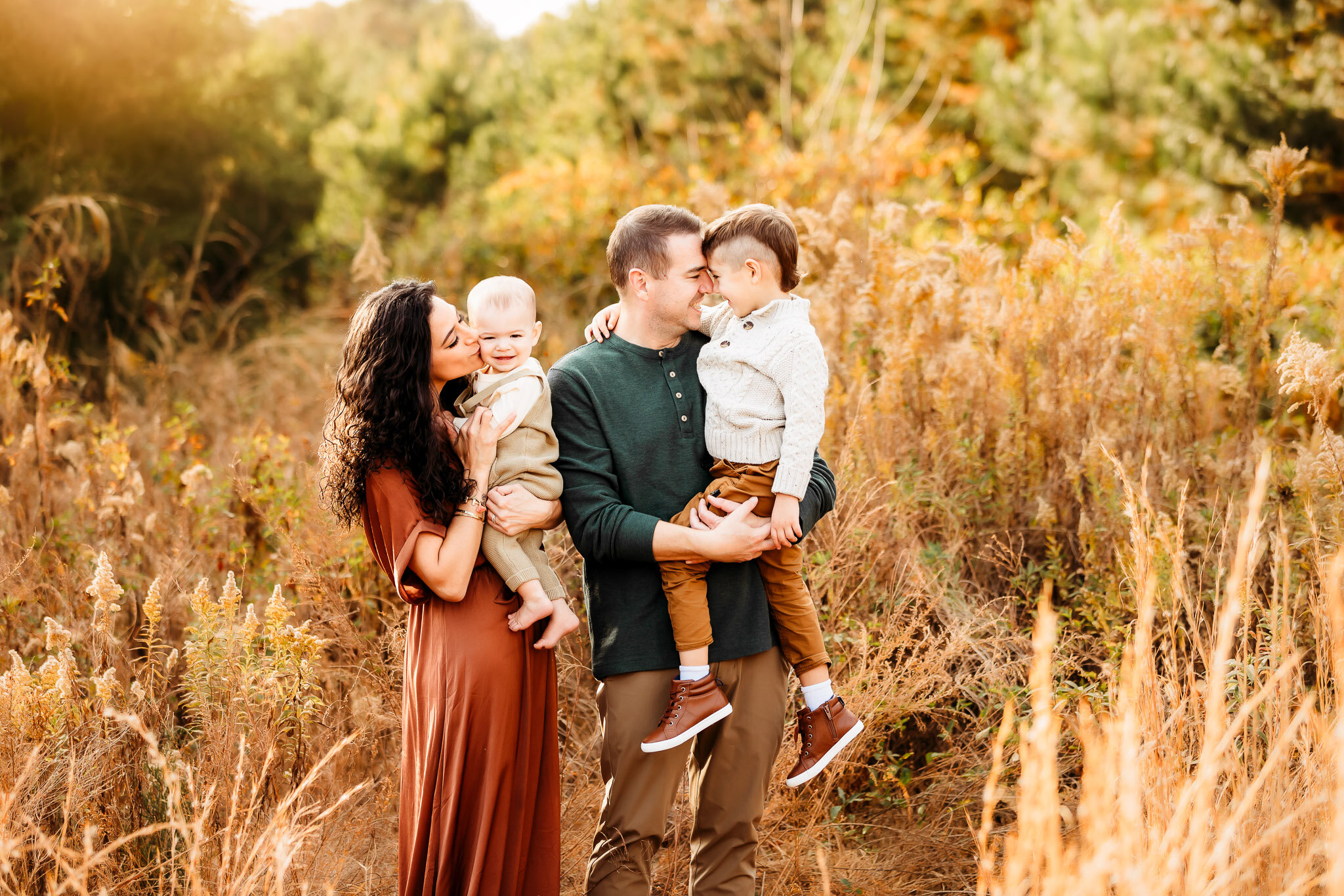 Parents in rust and deep green holding their two little boys in tall golden grass