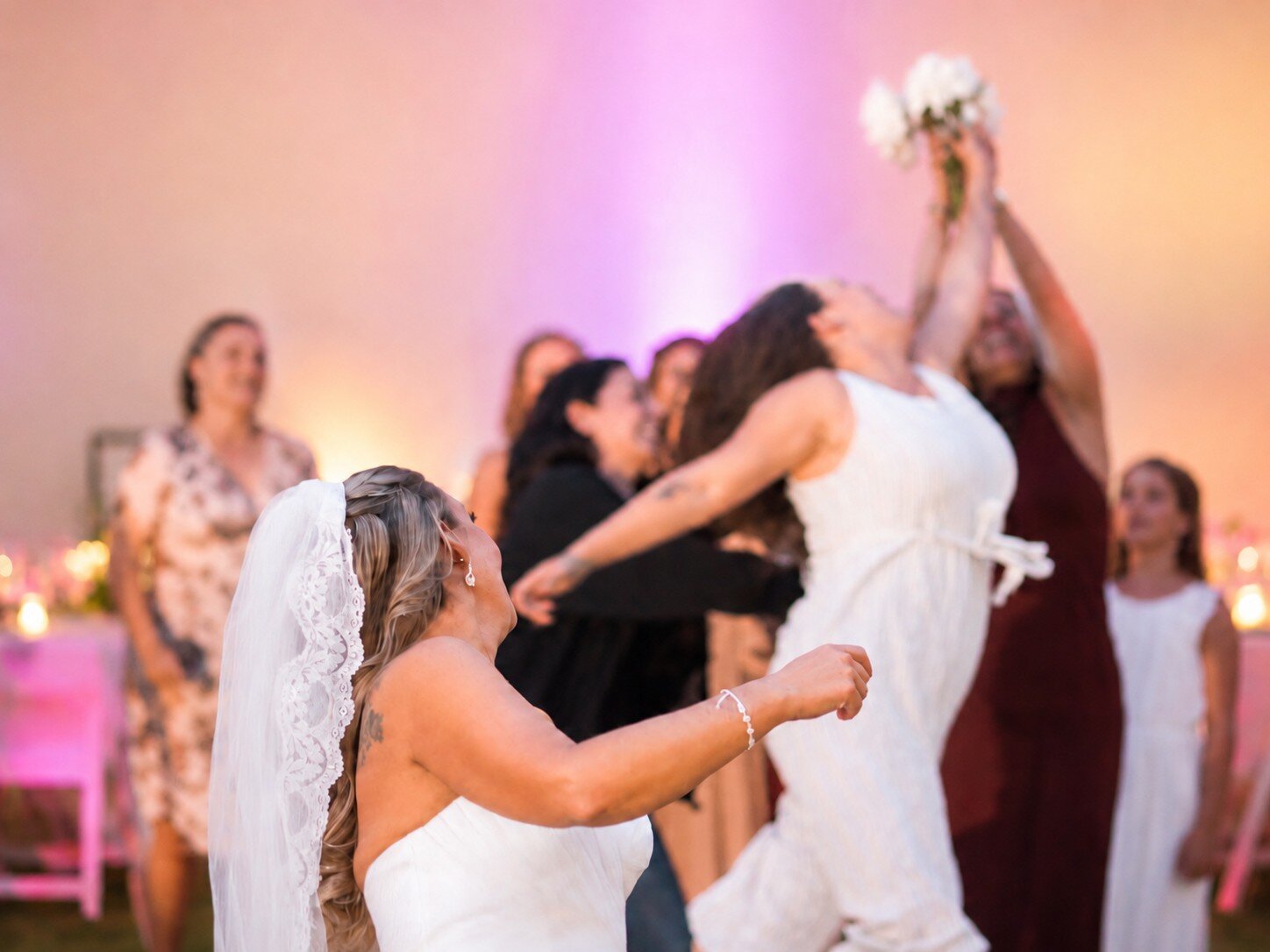Bride and wedding guests reacting during a lively bouquet toss at a reception