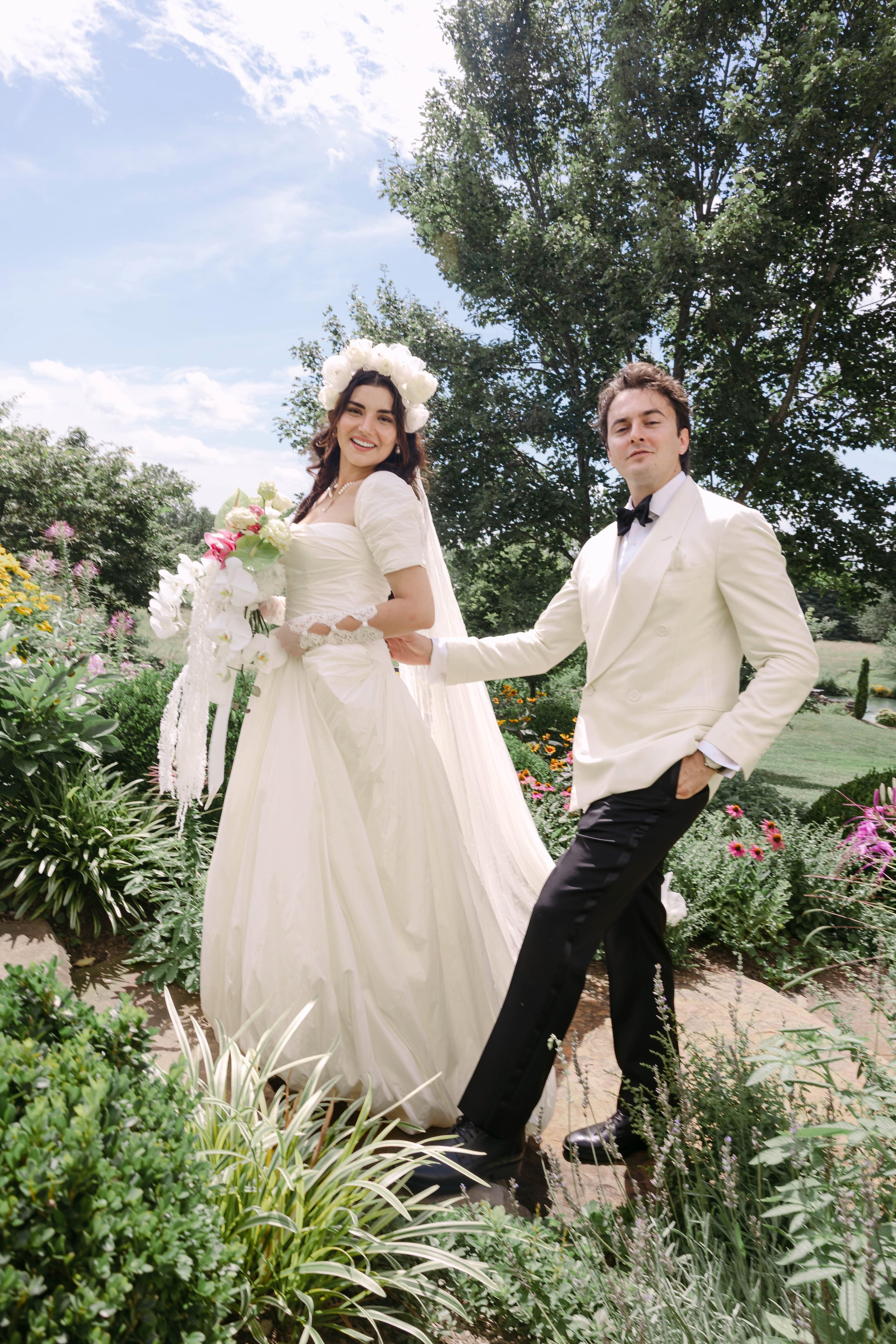 Bride and groom in a white dinner jacket walking through a lush garden at Missem and Ege's wedding