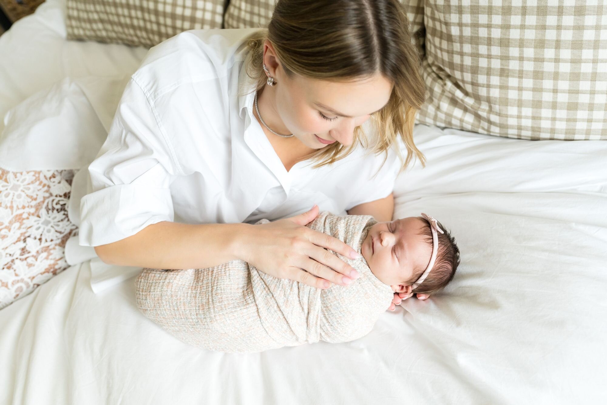 Mom gently resting her hand on her swaddled newborn on the bed