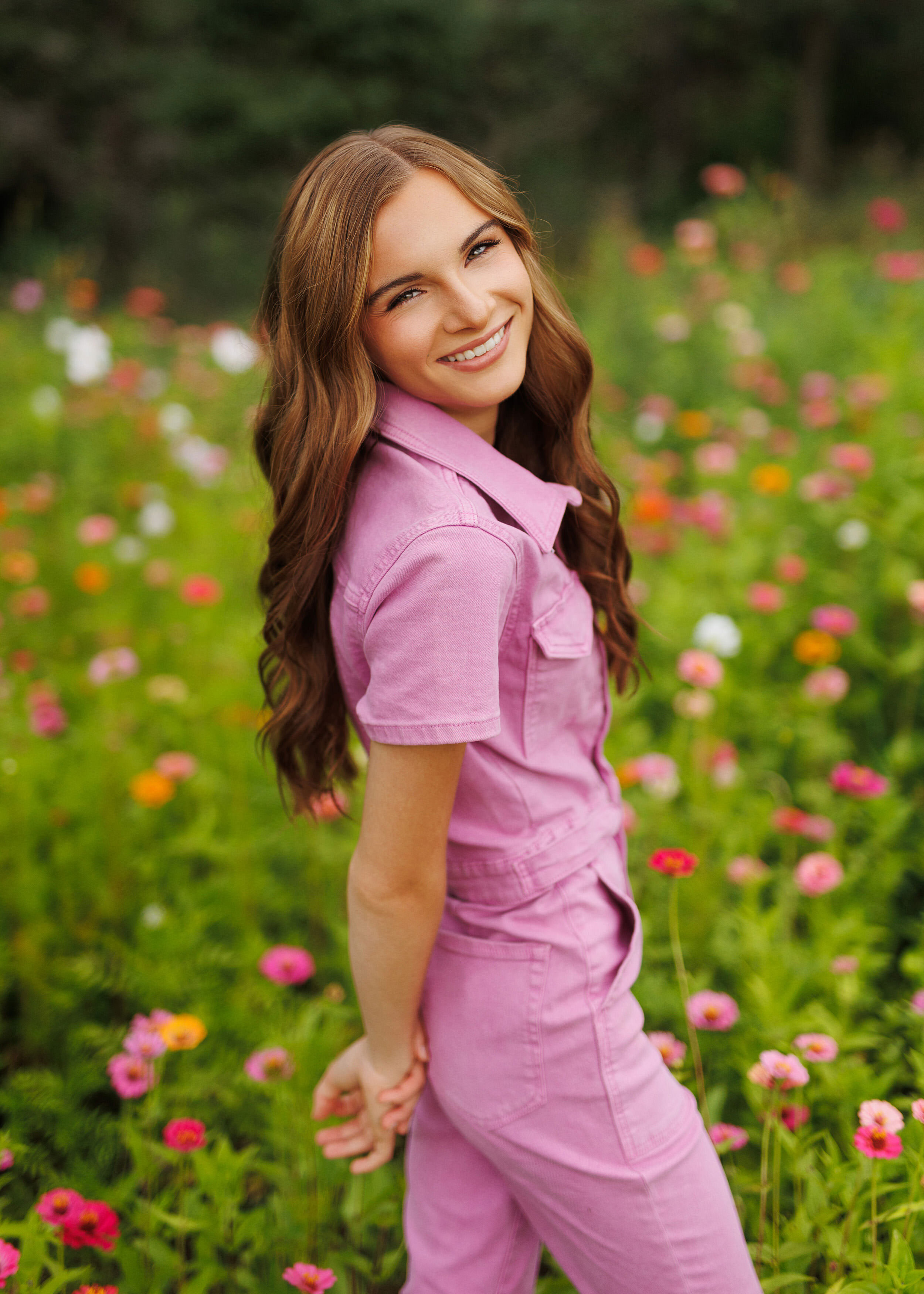girl in pink jumper posing in flowers during her outdoor senior pictures in minnesota