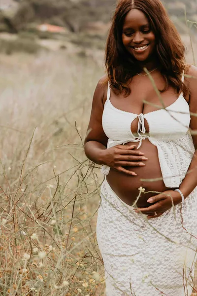 Close up of hands resting on a pregnant belly in a lace dress among golden grass in Los Angeles