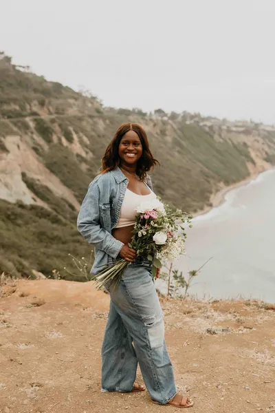 Pregnant woman in a teal dress holding a bouquet on a coastal bluff in Palos Verdes, California
