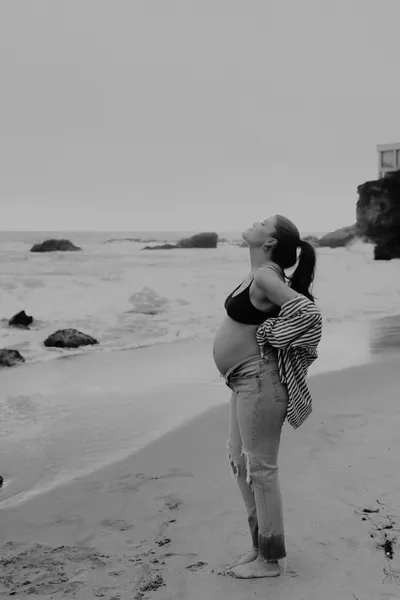 Pregnant woman walking the shoreline in a dark maternity gown