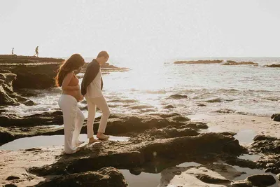 Couple standing on a tide pool reef shelf at sunset during a coastal maternity session in Orange County