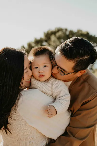 Parents holding their baby beneath a windswept pine on a Los Angeles hillside