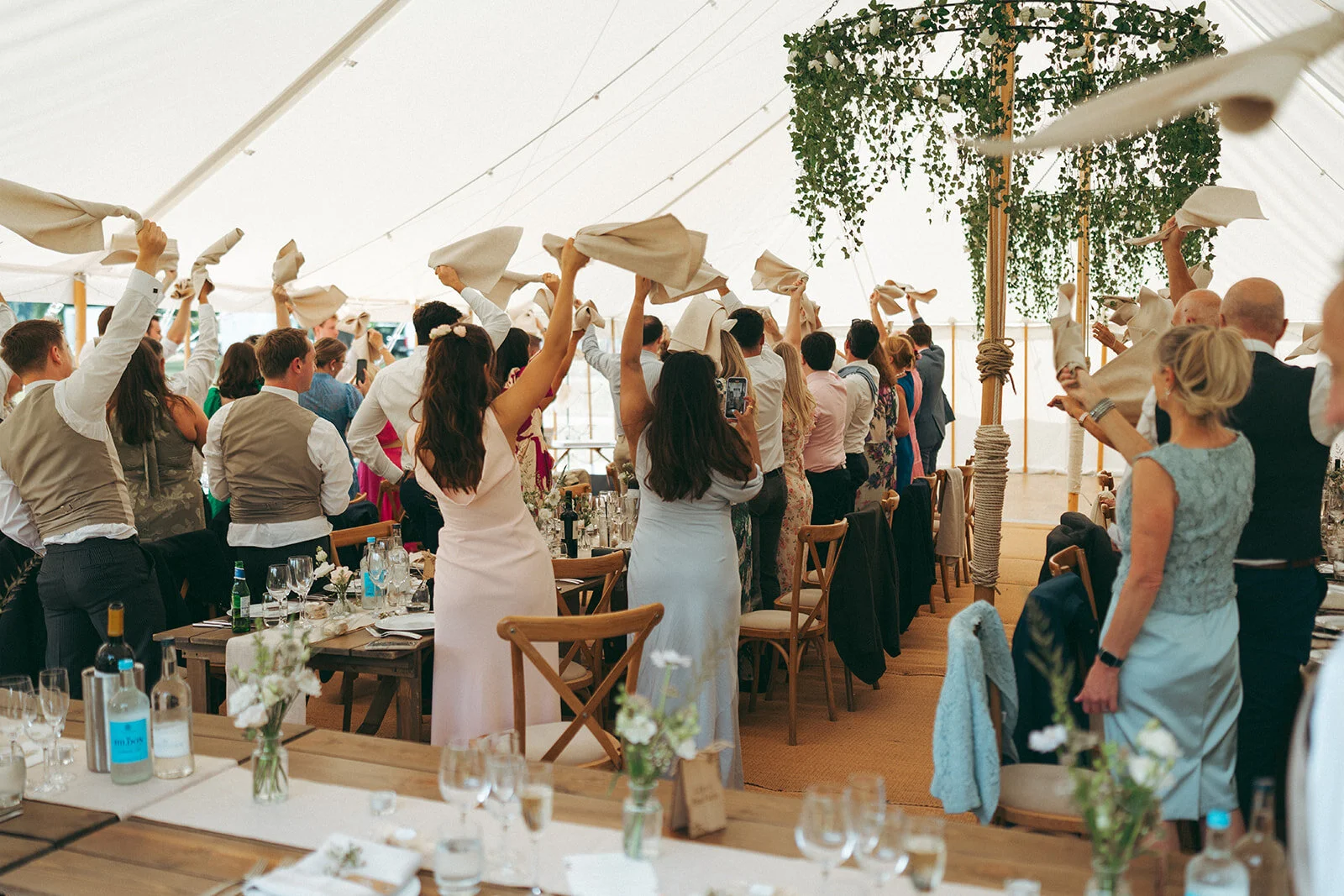 Guests waving napkins as the couple walk into the marquee