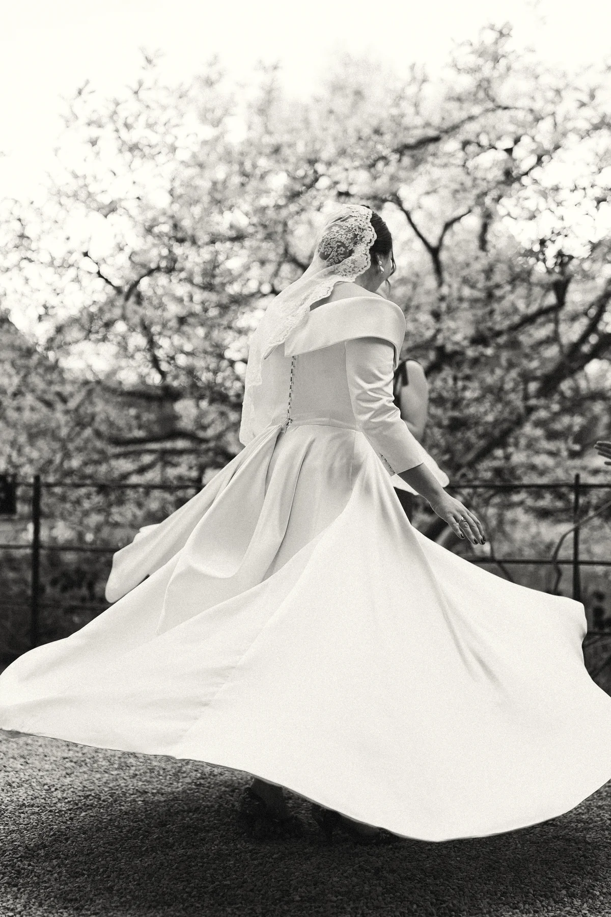 Bride spinning in her dress beneath blossom, on black and white film