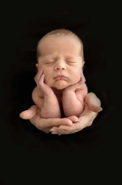 Sleeping newborn supported in an adult’s hands against a black background