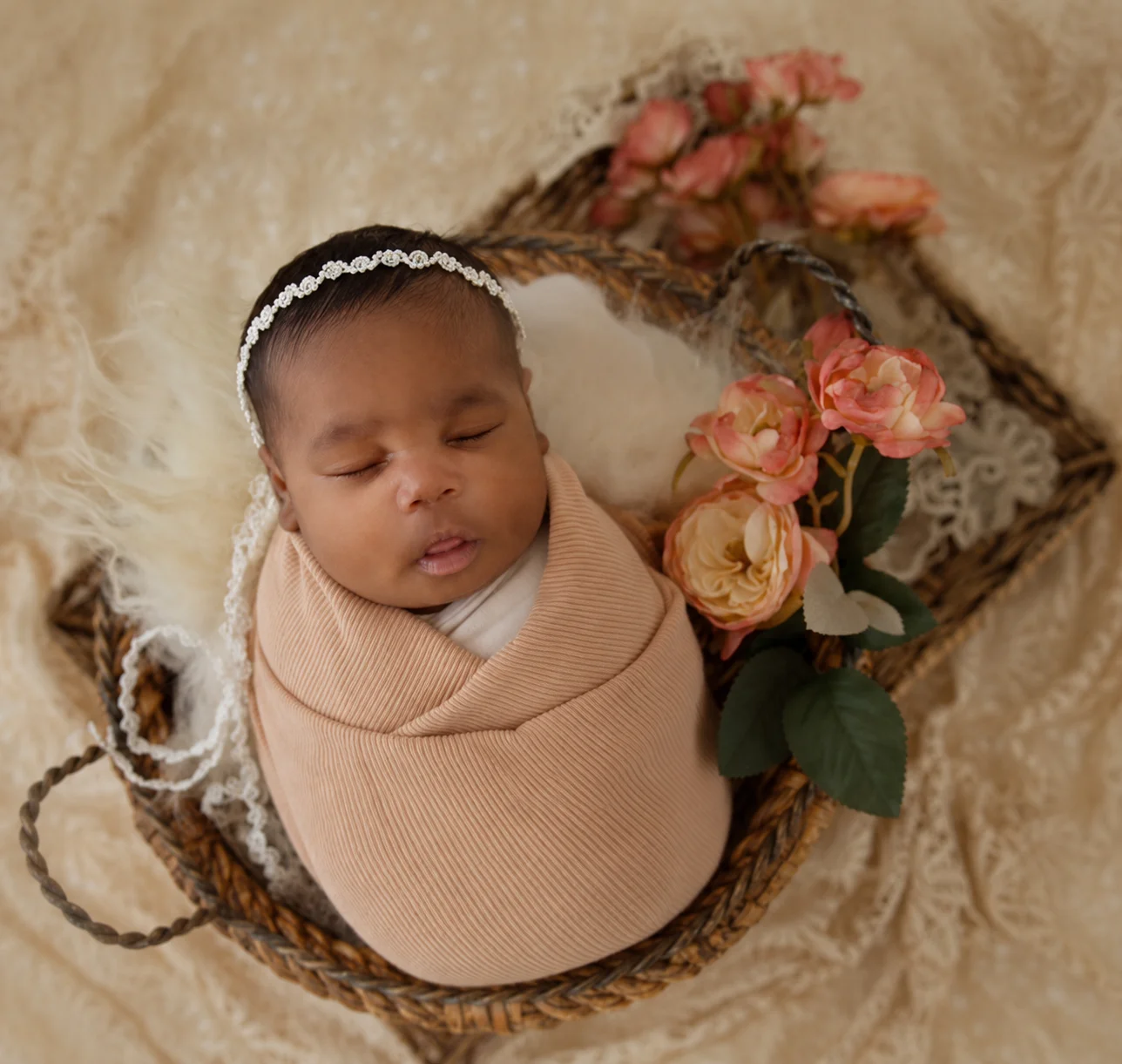 Newborn in a beige wrap, resting in a floral basket