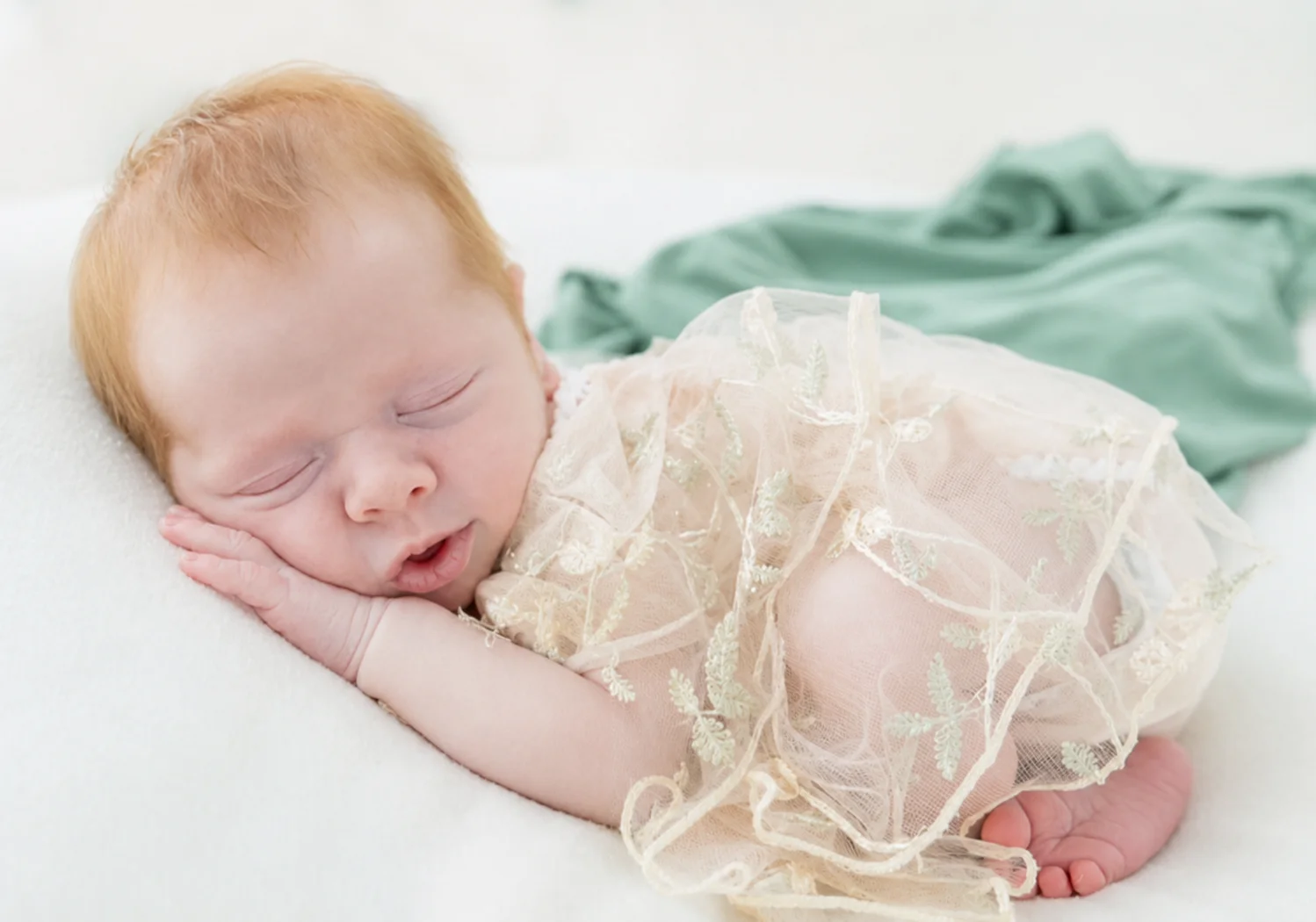 Sleeping newborn in delicate lace on cream bedding with a green blanket