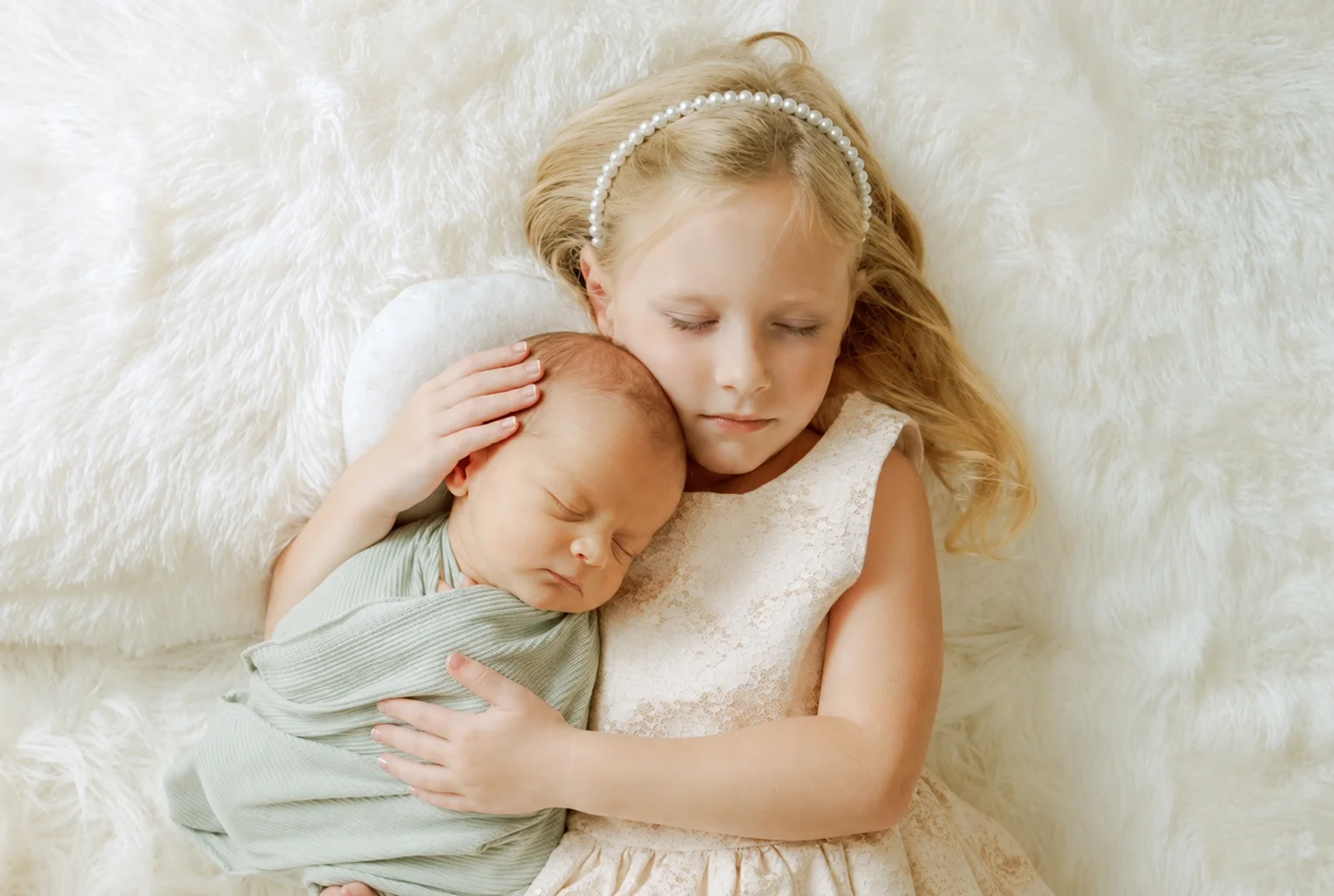 Older sister holding a newborn wrapped in soft green